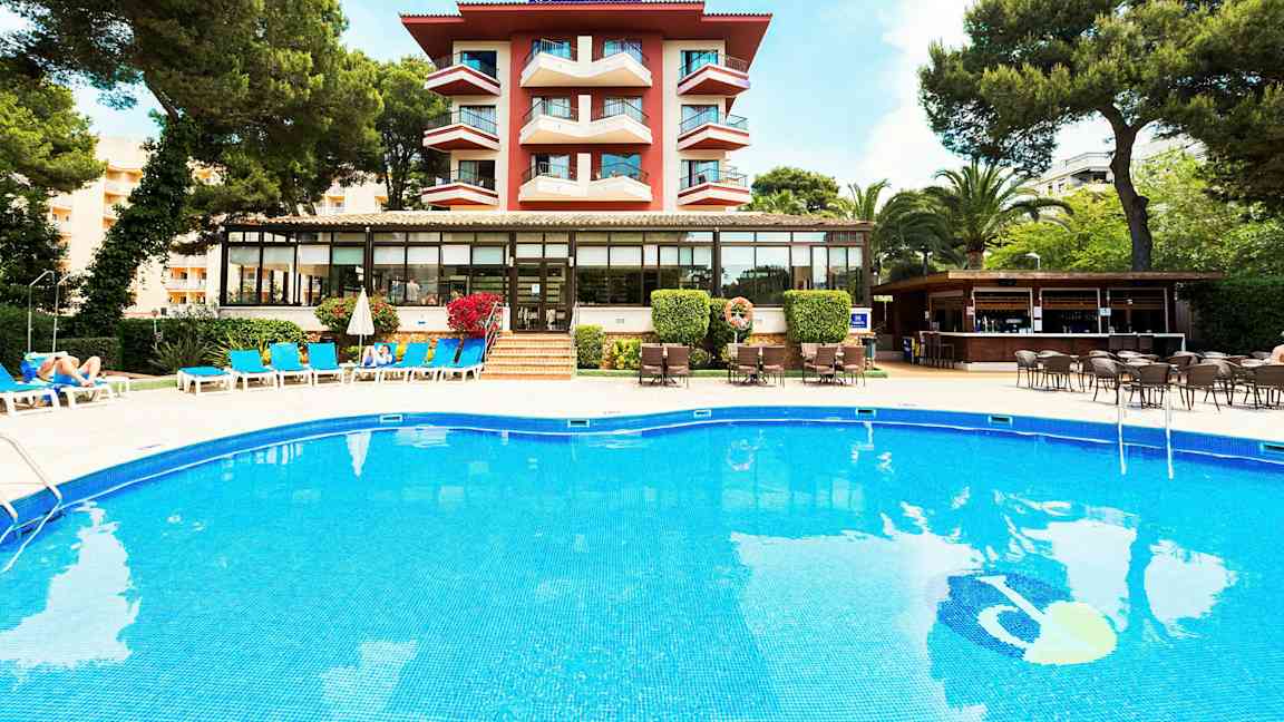 Byggnad med balkonger, pool och solstolar framför, omgiven av grönska. (AI-genererad text)