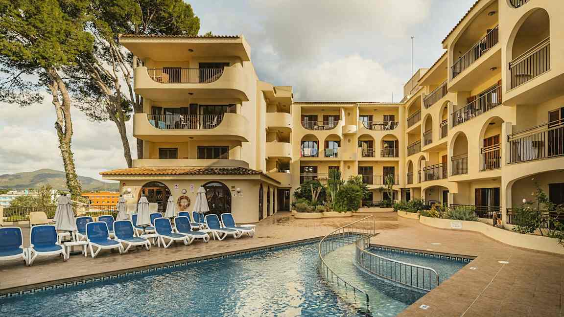 En bild av en hotellbyggnad med flera våningar, en pool och solstolar framför. (AI-genererad text)