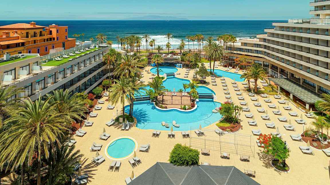 En hotellanläggning med pooler, solstolar och palmer, nära havet. (AI-genererad text)