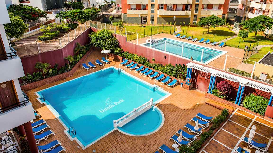 Ett hotellområde med två pooler, solsängar och omgivande byggnader. (AI-genererad text)