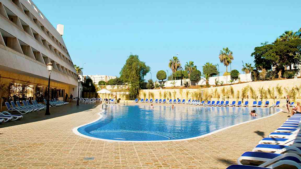 En hotellpool med solstolar runt omkring. (AI-genererad text)