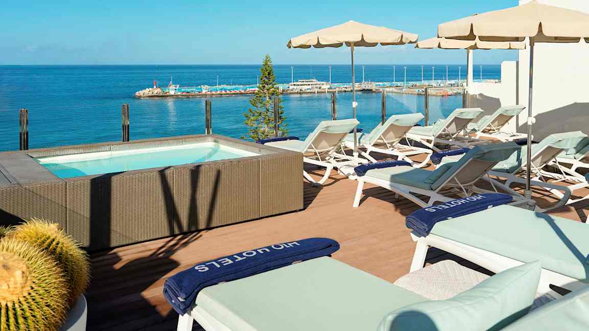 Terrass med solstolar och parasoller vid en jacuzzi med havsutsikt. (AI-genererad text)