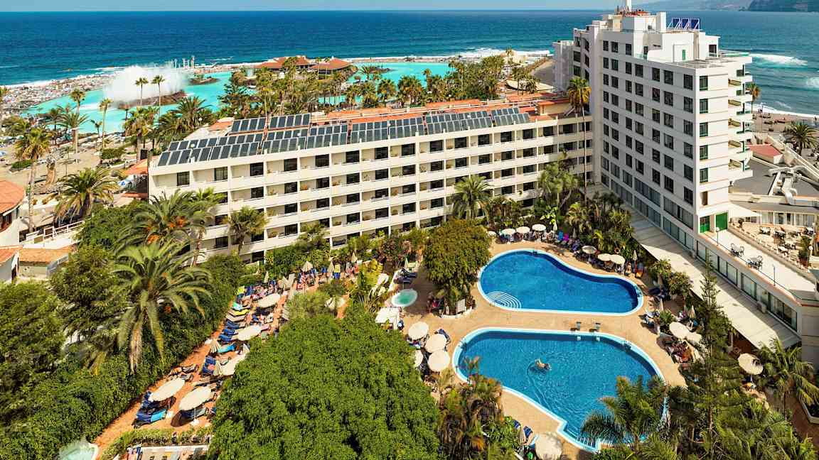 Hotellanläggning med pooler och grönska nära havet. (AI-genererad text)