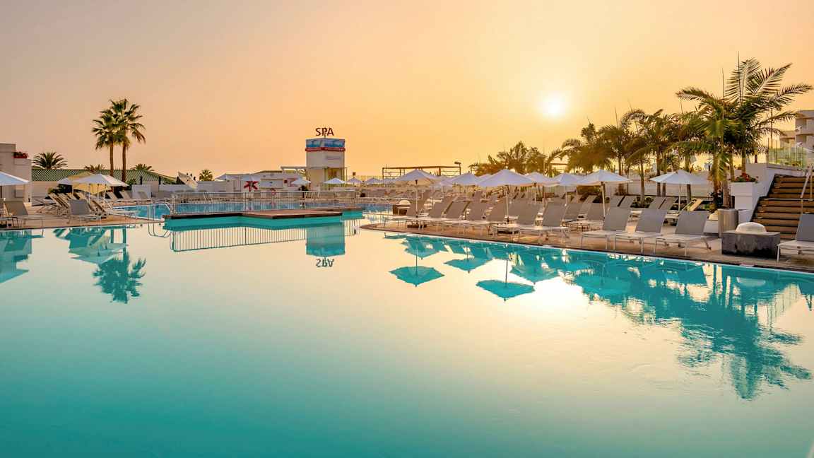 Poolområde med solstolar och parasoller vid solnedgången. (AI-genererad text)