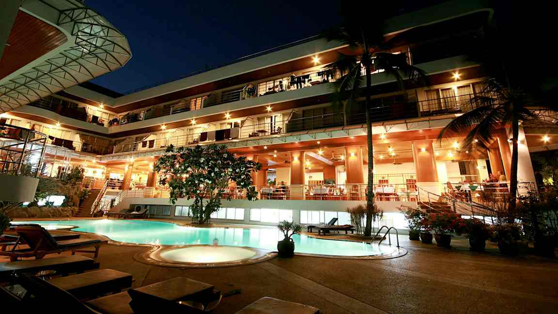 Kvällsvy av en byggnad med flera våningar, lysande fasad och en pool i förgrunden. (AI-genererad text)