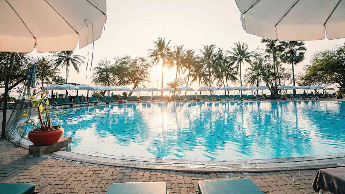 En solig dag vid en pool med parasoll och palmer i bakgrunden. (AI-genererad text)