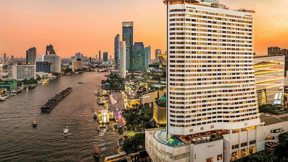 Vy över en flod som omges av höghus under en solnedgång. Ett stort hotell är synligt i förgrunden. (AI-genererad text)