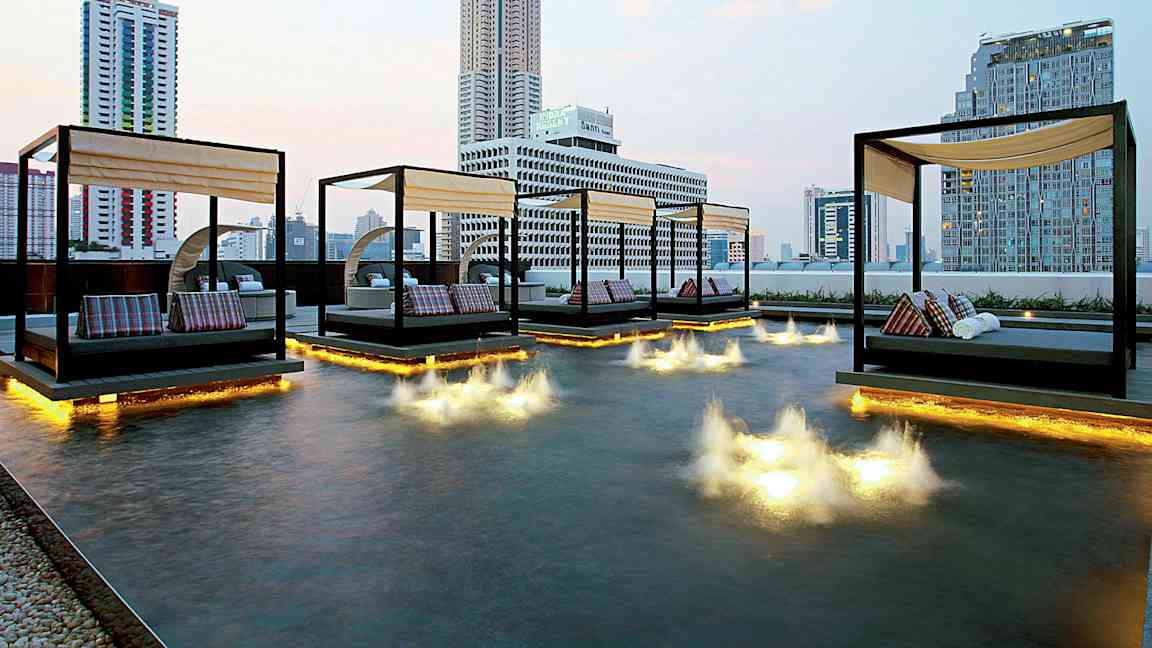 Bild av en modern stadsutsikt med dagbäddar som står ovanpå en grund pool med ljusinstallationer i vattnet. (AI-genererad text)