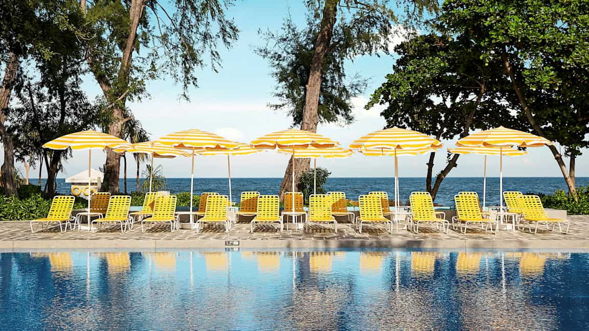 En pool framför solstolar med gula och vita parasoller nära stranden. (AI-genererad text)