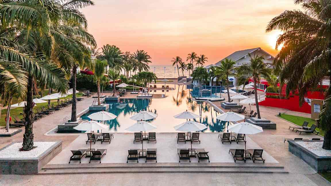 En pool med solstolar och parasoller vid solnedgång. (AI-genererad text)