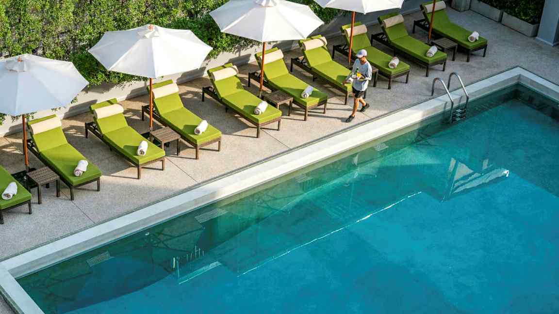 Pool med solstolar och parasoller vid kanten, samt en person som går förbi. (AI-genererad text)