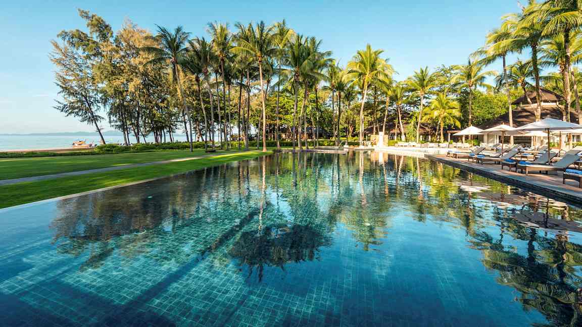 En utomhuspool omgiven av grönska och palmer, med utsikt över stranden och havet. (AI-genererad text)