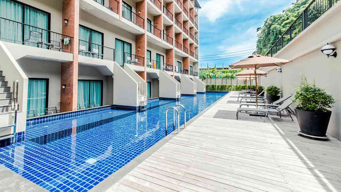 Ett hotell med flera våningar och en lång pool framför byggnaden, omgiven av solstolar och parasoller. (AI-genererad text)
