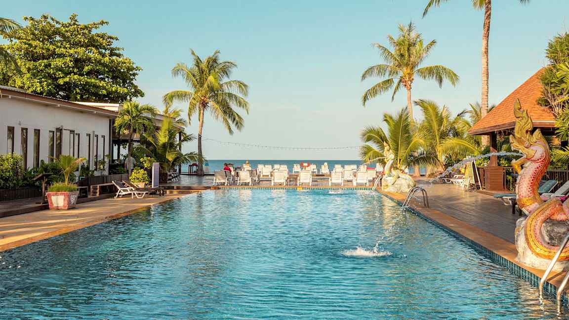 Utomhuspool med palmer och solsängar i bakgrunden, samt en dekoration föreställande en drake bredvid poolen. (AI-genererad text)