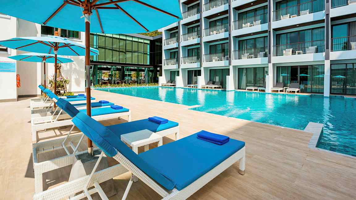 En swimmingpool på ett hotell med solstolar och parasoller i förgrunden. (AI-genererad text)