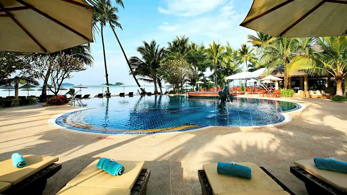 En pool omgiven av palmer och solstolar med utsikt mot havet och en blå himmel. (AI-genererad text)