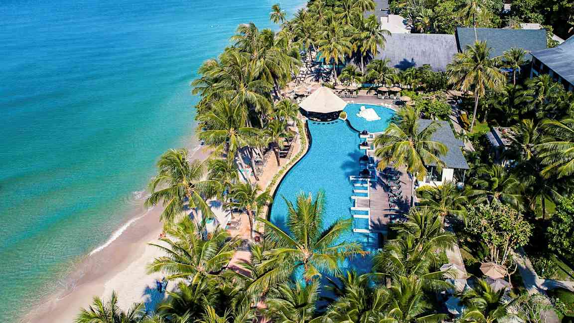 Flygbild över en strandresort med pool, solstolar och palmer nära havet. (AI-genererad text)