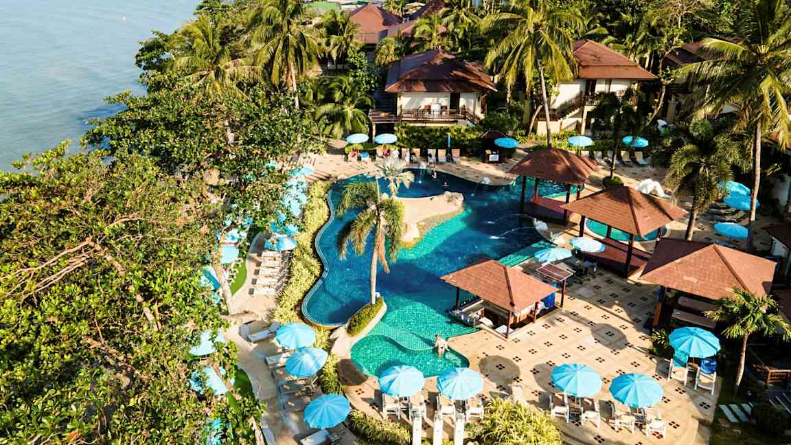 En resort med pool, palmer och parasoller vid havet. (AI-genererad text)