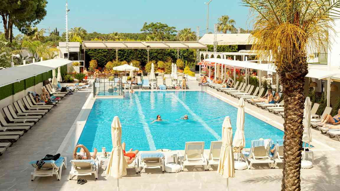 Bild av en pool omgiven av solstolar och parasoller, med personer som badar och solar. (AI-genererad text)