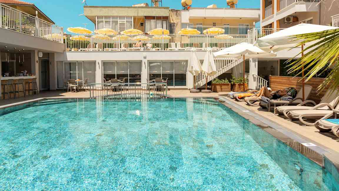 En utomhuspool omgiven av solstolar och parasoller på ett hotell. (AI-genererad text)