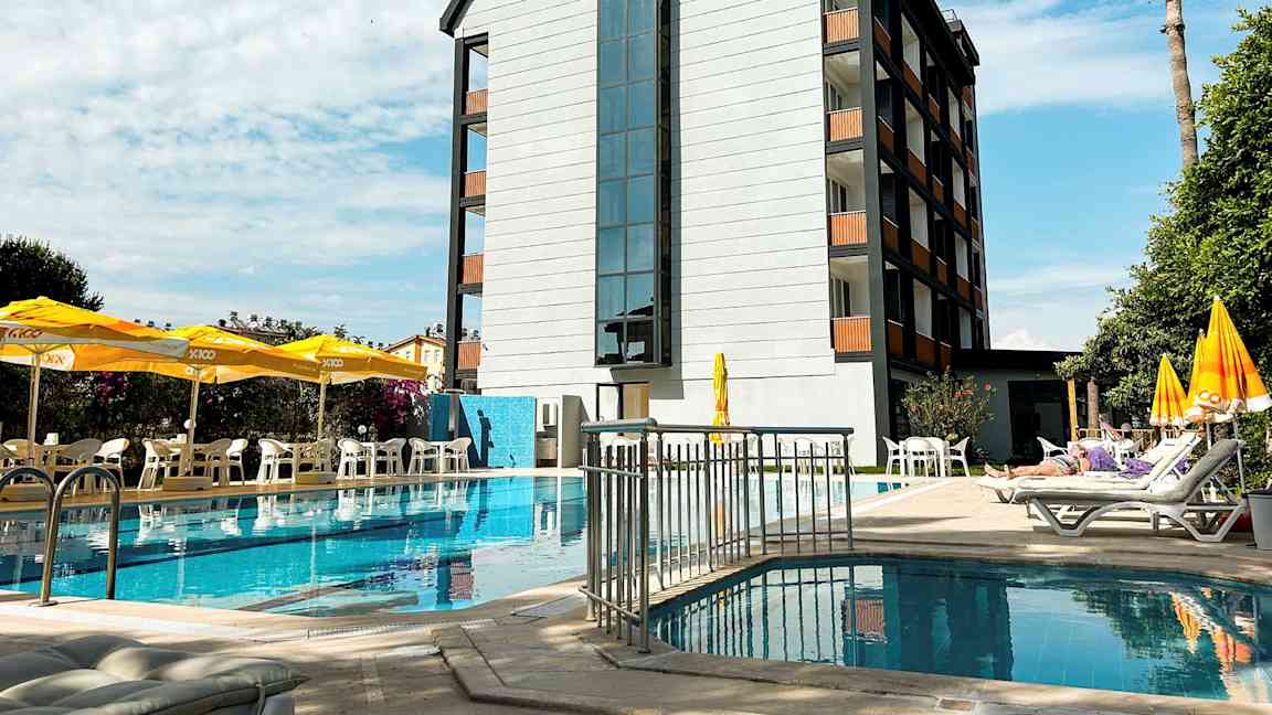En byggnad vid en pool med solstolar och parasoller på terrassen. (AI-genererad text)