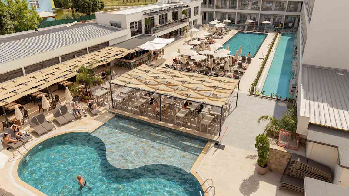 Hotellets poolområde med solstolar, parasoller och en servering vid poolen. (AI-genererad text)