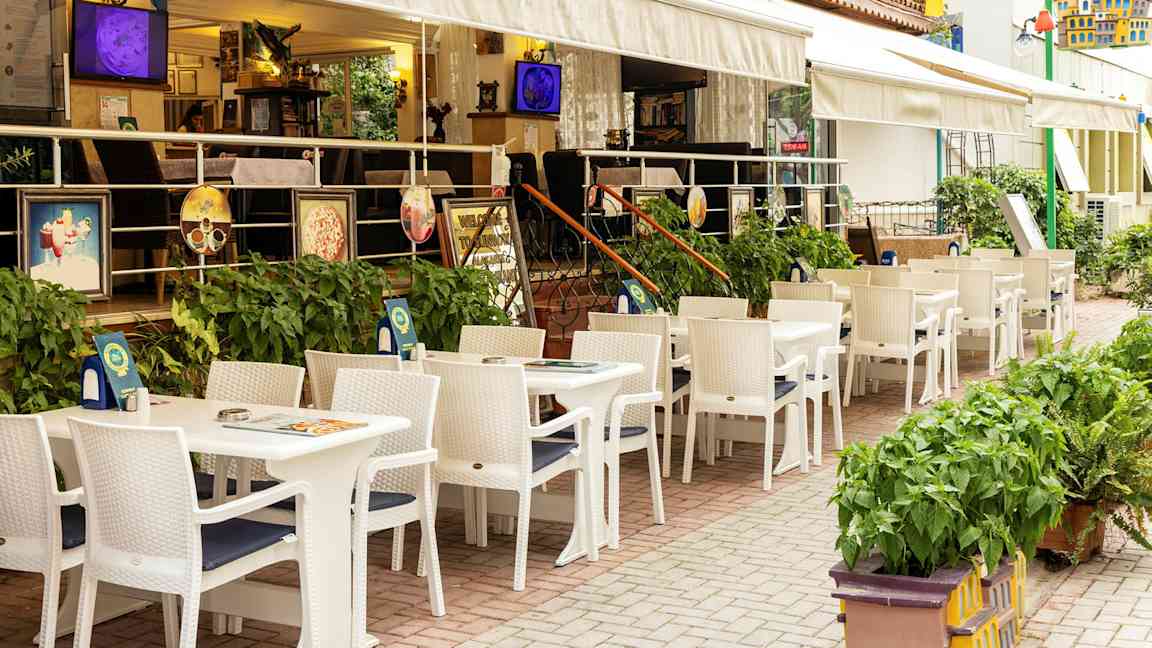 Restaurang med uteservering med vita bord och stolar vid ett hotell. (AI-genererad text)