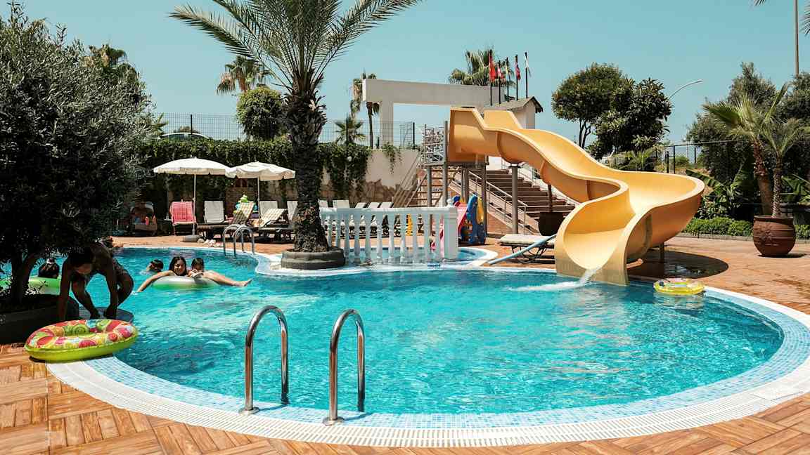 En swimmingpool med en gul vattenrutschkana och omgivna av palmer. (AI-genererad text)