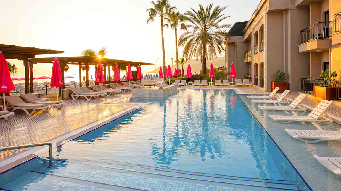 Pool med solstolar och parasoller, omgiven av palmer vid solnedgång. (AI-genererad text)