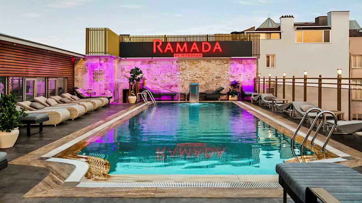 Bild av en utomhuspool med solstolar runt om och ett skylt med texten Ramada by Wyndham. (AI-genererad text)