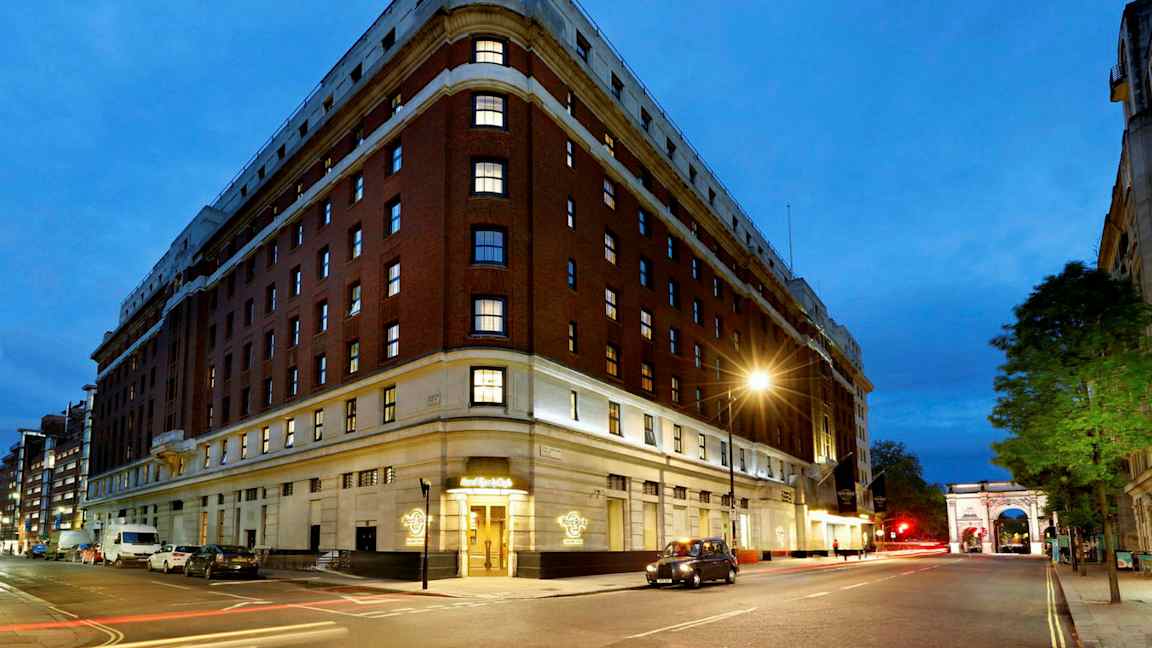 En stor byggnad med tegelväggar och flera våningar, synlig på natten med gatulampor och trafikljus. En båge står längre ner på gatan. (AI-genererad text)