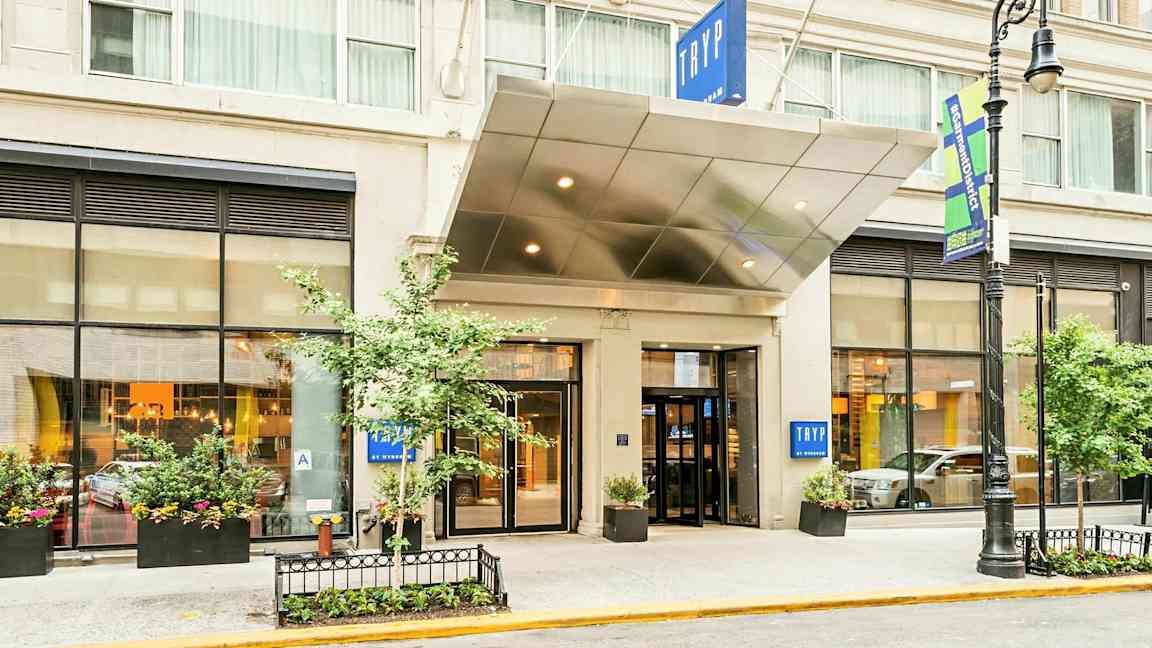 Entré till ett hotell med skylt texten "TRYP". Byggnaden har stora fönster och planteringar. (AI-genererad text)