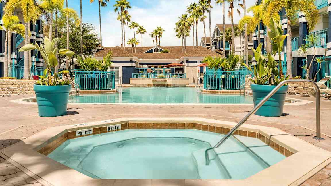 Bild av en pool med omgivande solstolar och palmer. I förgrunden ett mindre bubbelbad med poolräcke. (AI-genererad text)