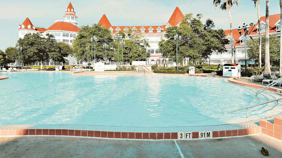 Bild av en pool med ett elegant vitt hotell med röda tak i bakgrunden. (AI-genererad text)