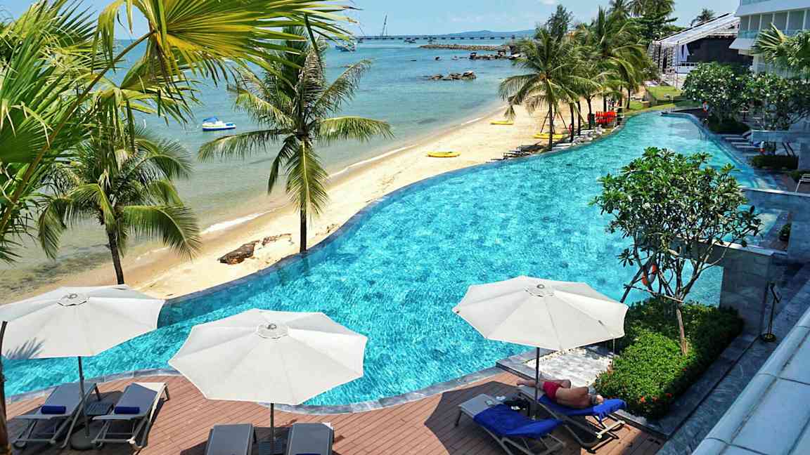 En strand med palmer och en pool i förgrunden. (AI-genererad text)