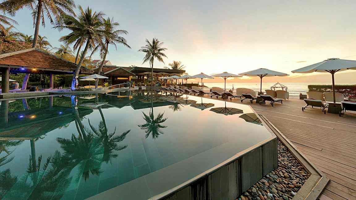 En pool med utsikt över havet omgiven av palmträd och solstolar. (AI-genererad text)