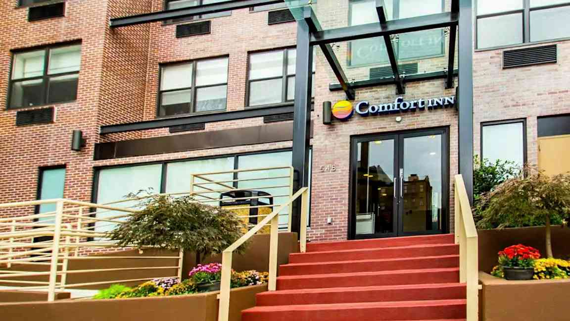 Entrén till en byggnad med texten "Comfort Inn" ovanför dörren. (AI-genererad text)