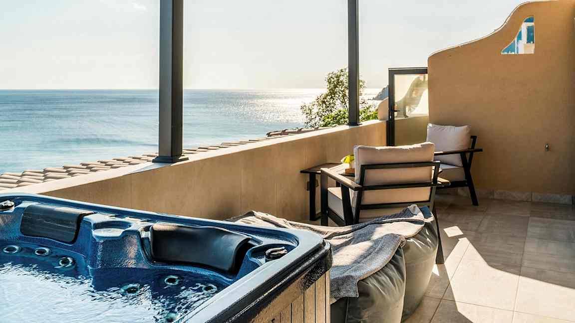 En terrass med en jacuzzi, sittmöbler och utsikt över havet under en takpergola. (AI-genererad text)