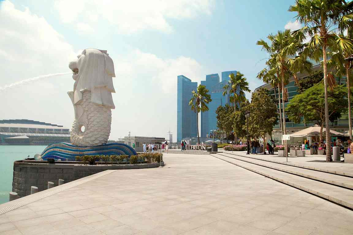 Bild på Merlion-statyn i Singapore med fontän, omgiven av modern arkitektur och palmer. (AI-genererad text)