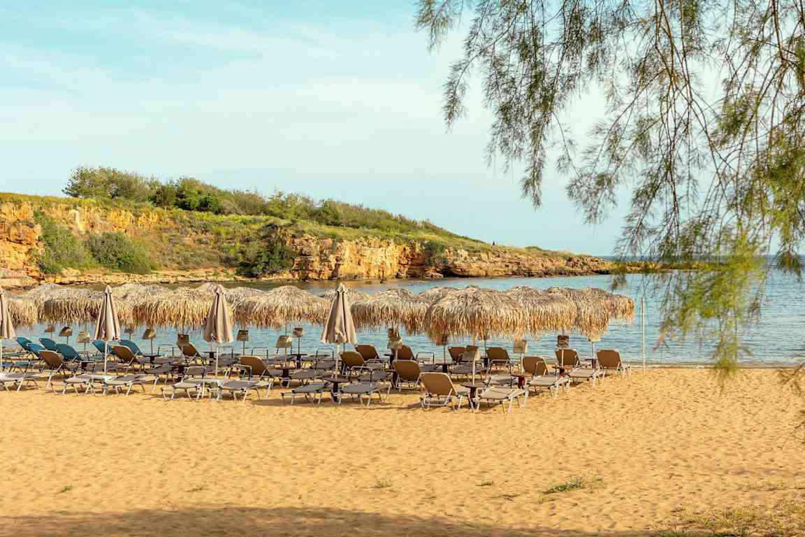 En strand med solstolar och parasoller av halm framför havet. (AI-genererad text)