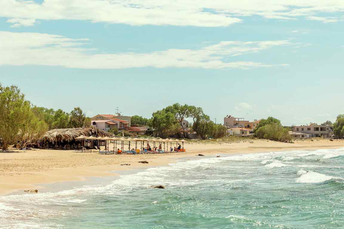 En strand med havsutsikt, parasoller och små byggnader i bakgrunden. (AI-genererad text)