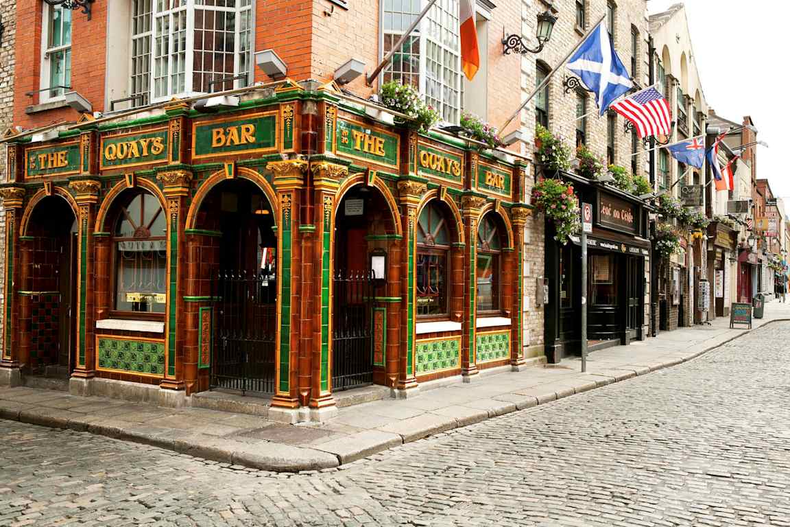 En färgglad pub med grön och orange dekor i traditionell stil ligger vid en kullerstensgata. (AI-genererad text)