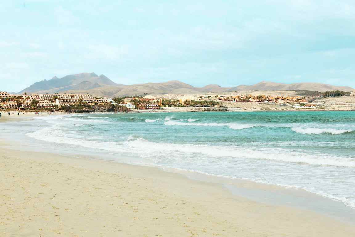 En sandstrand med vågor och hotellbyggnader i bakgrunden. (AI-genererad text)