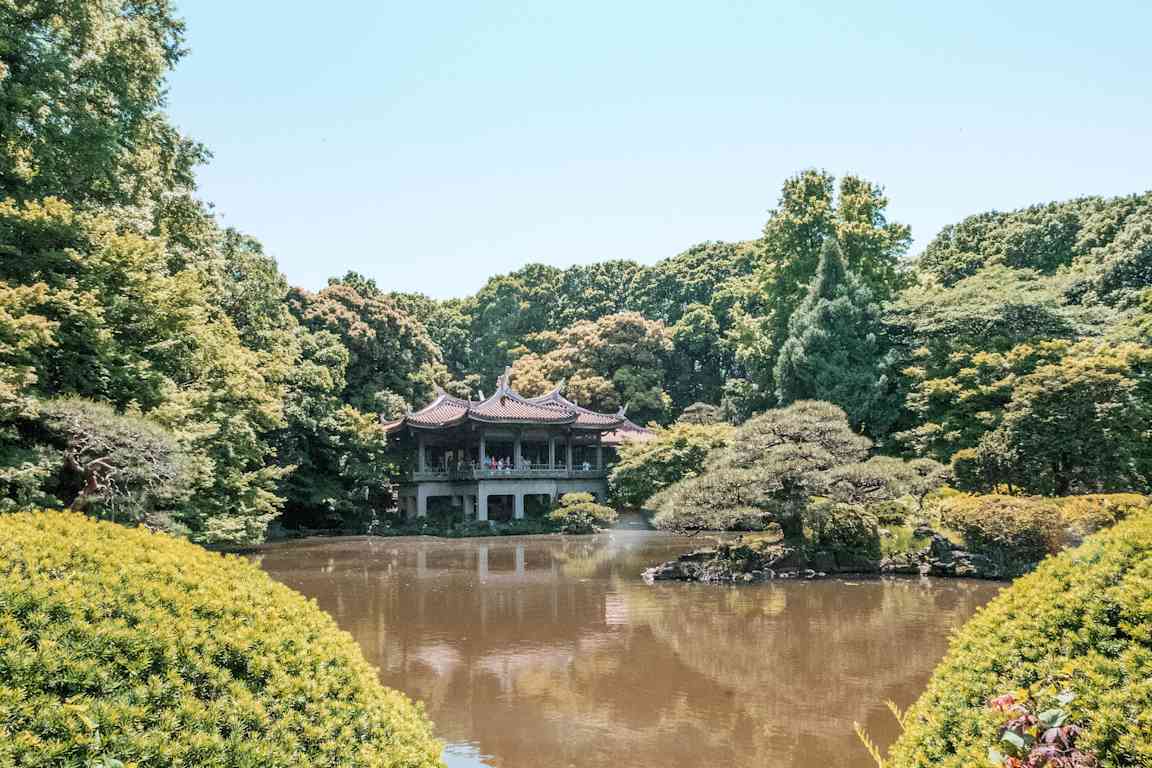 En kinesisk paviljong vid en damm i en grönskande park. (AI-genererad text)