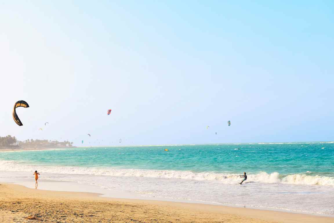 En strand med turkost hav och många kitesurfare. (AI-genererad text)
