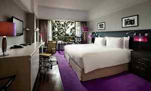 Hotellrum med en stor säng och modern inredning, skrivbord och stol samt en utsikt genom ett stort fönster. (AI-genererad text)