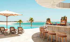 En pool vid stranden med solstolar, parasoll och en poolbar med exotiska frukter. (AI-genererad text)