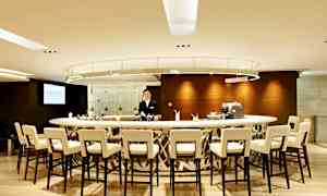 En modern bar med ett runt bardiskområde, omgiven av stolar. En person står bakom bardisken. (AI-genererad text)