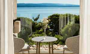 En borddekoration med blommor vid ett bord framför fönster med utsikt över havet och grönska. (AI-genererad text)