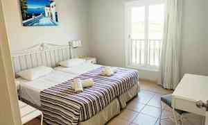 Ett hotellrum med två enkelsängar, dekorerade med randiga överkast och handdukar. Ett fönster och en skrivbordshörna är synliga. (AI-genererad text)